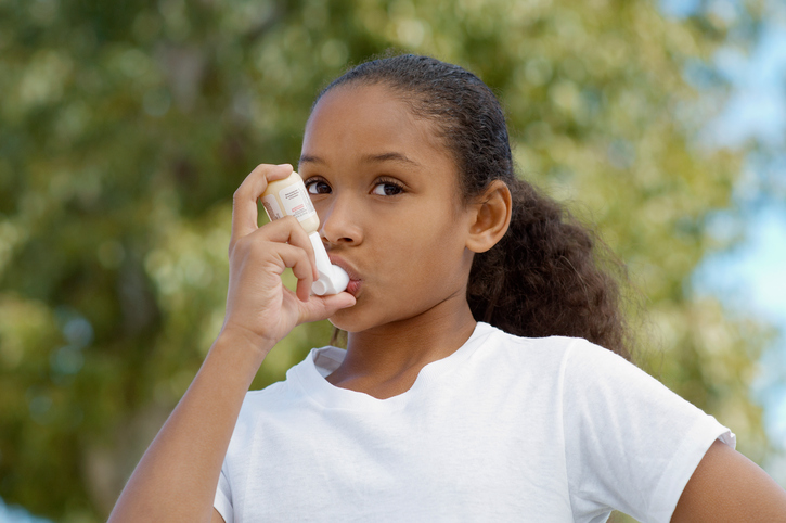 Girl (7-9) using inhaler, outdoors